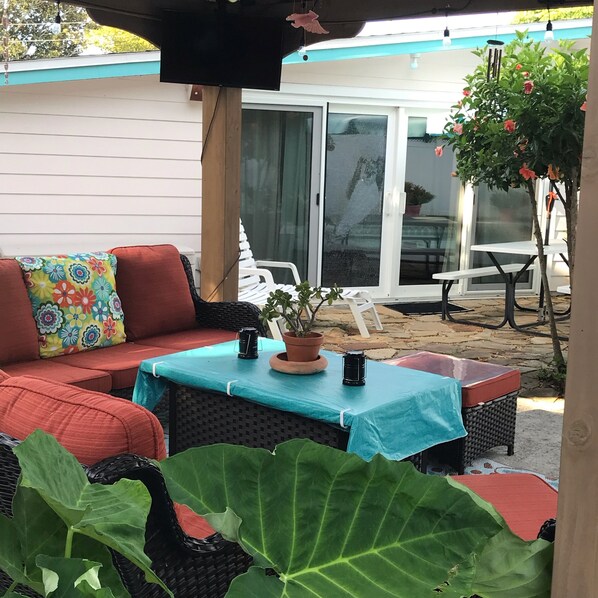 Un espace patio aménagé avec un canapé en osier, une table recouverte d’une nappe bleue et une plante en pot.