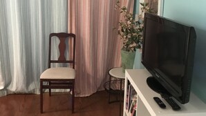 Una sala de estar con una silla de madera, un televisor sobre un mueble blanco y una cortina a rayas.