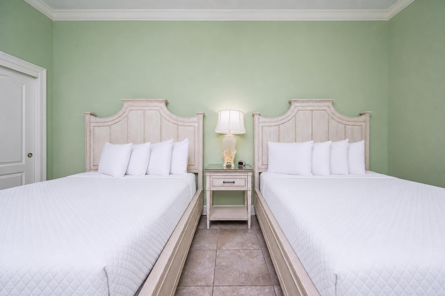 Une chambre avec deux lits, une table de chevet avec une lampe et une porte.