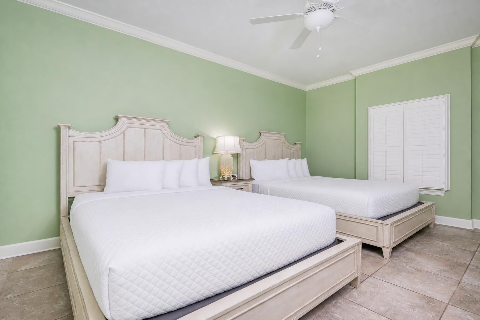 Een slaapkamer met twee bedden, een plafondventilator en een raam met luiken.
