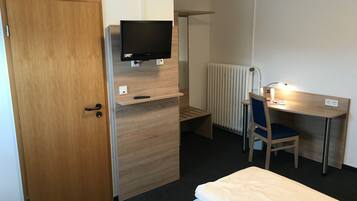 Habitación de hotel con puerta de madera, televisor montado en un estante de madera, escritorio con una silla y una cama.