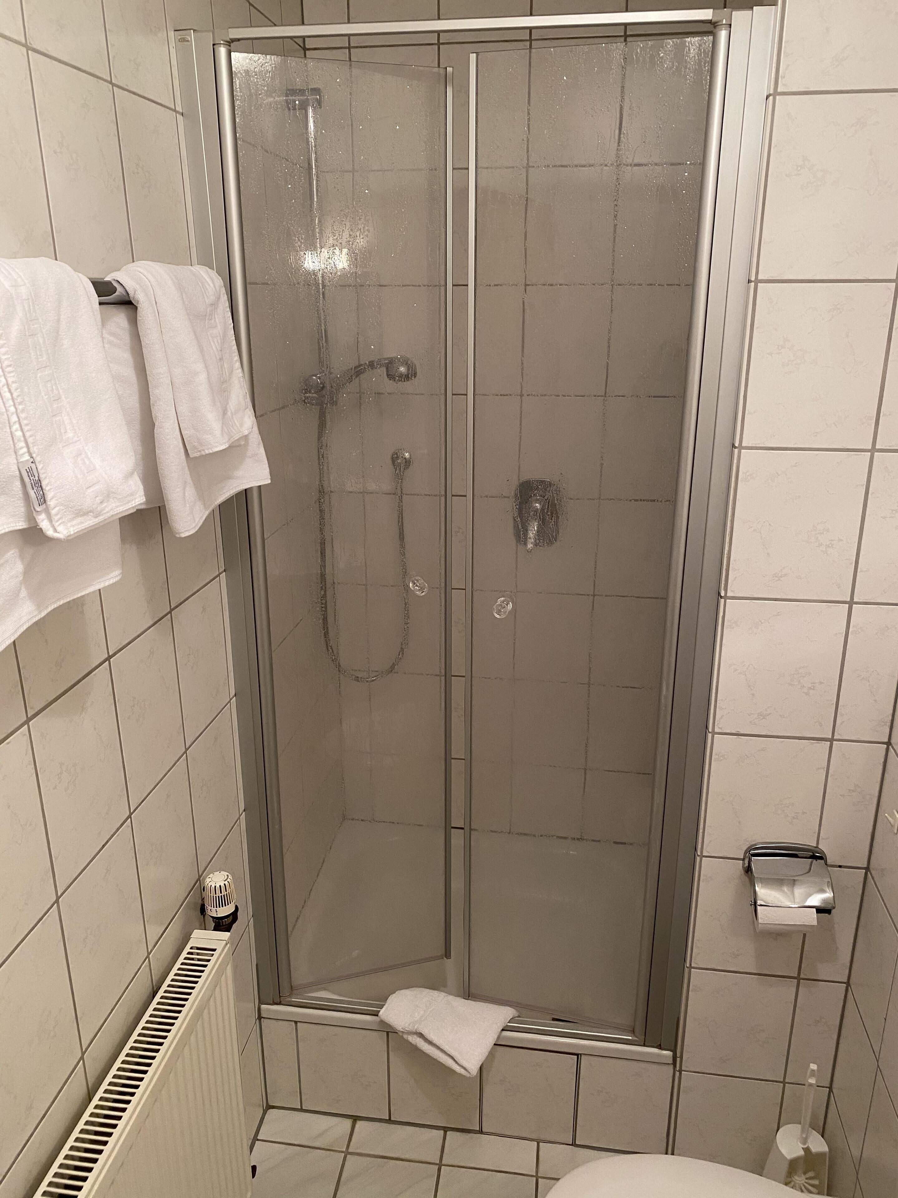 A shower area with a glass door, a towel rack with towels, a toilet paper holder, and a vent.