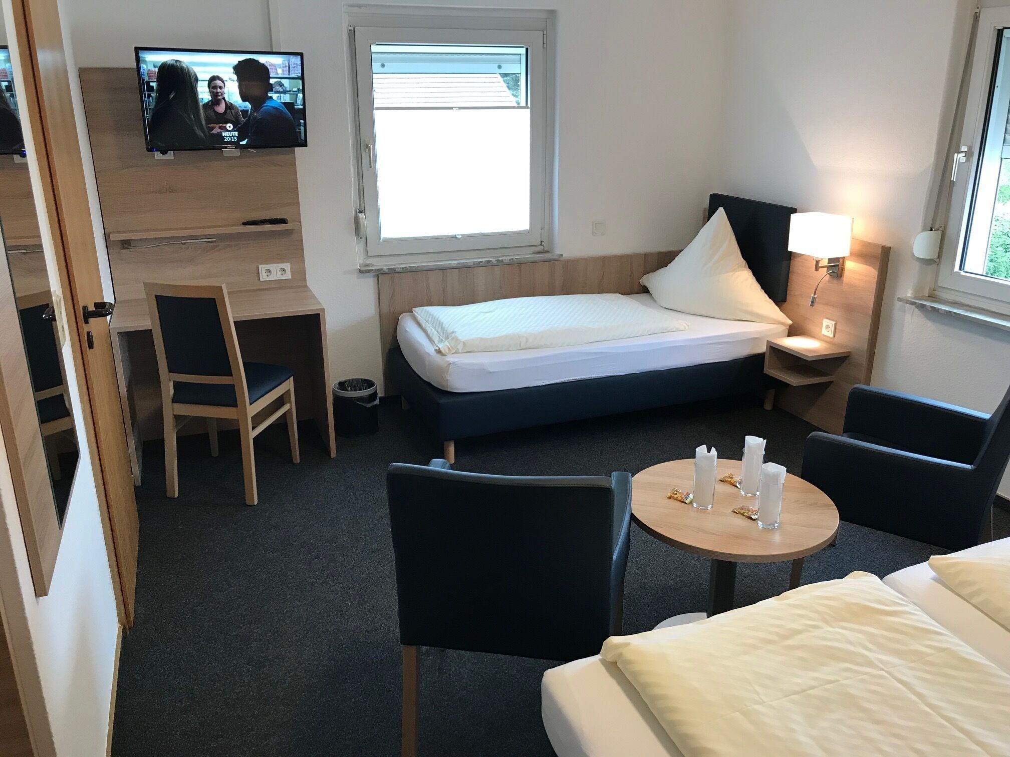 Ein Hotelzimmer mit einem Bett, einem Schreibtisch, einem Sessel, einem Fernseher und einem kleinen Tisch mit Tasse und Glas.