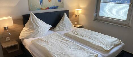 A hotel room with a neatly made double bed, a world map artwork on the wall, a bedside lamp, and a window with a view of the countryside.