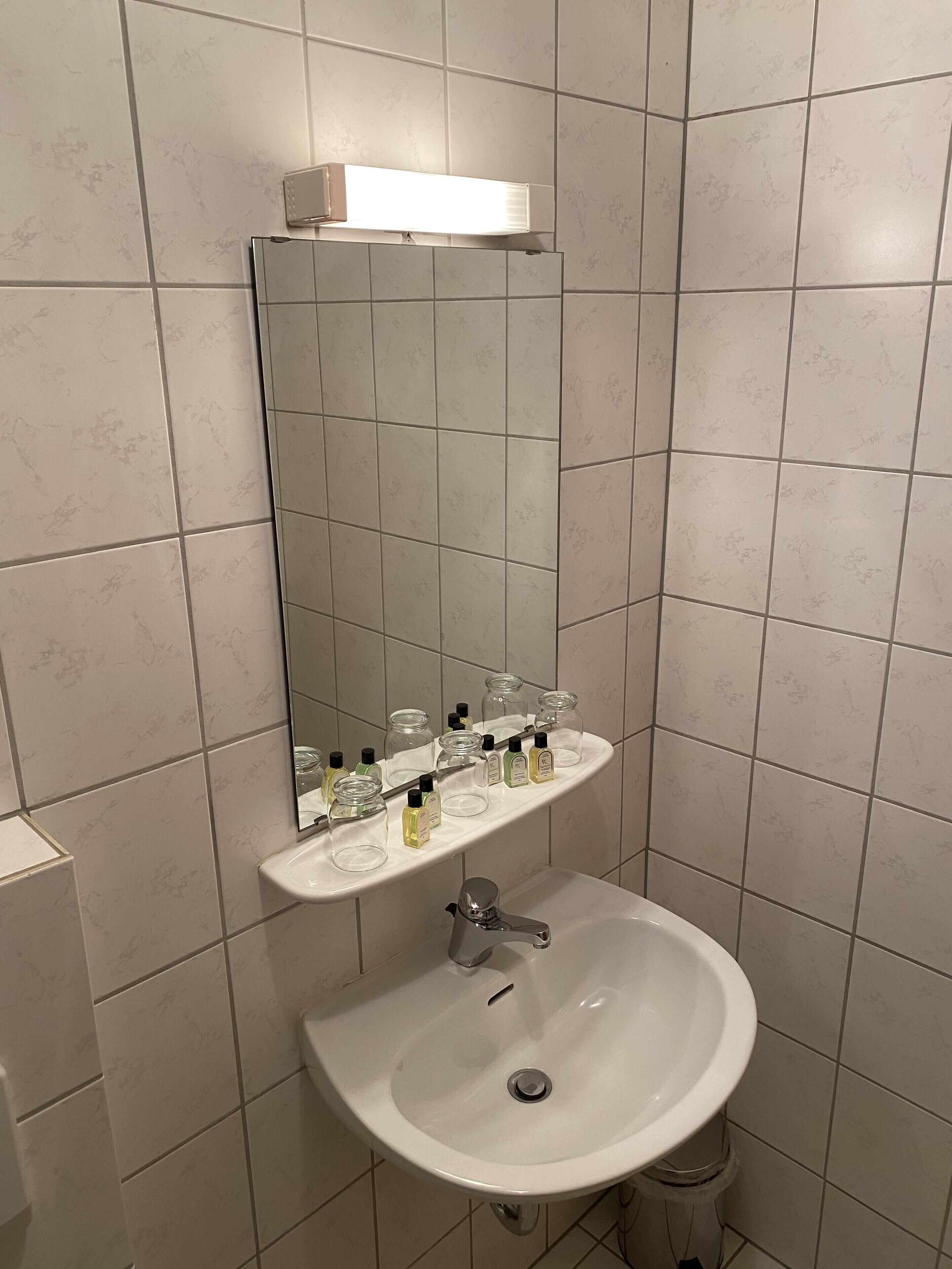 Un baño con un lavamanos blanco, un espejo y un estante con artículos de aseo.
