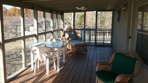 Un porche techado con una mesa y sillas, una silla de mimbre y vistas al exterior.