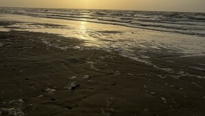 Una platja amb el sol ponent-se a l'horitzó, creant una atmosfera serena i tranquil·la.