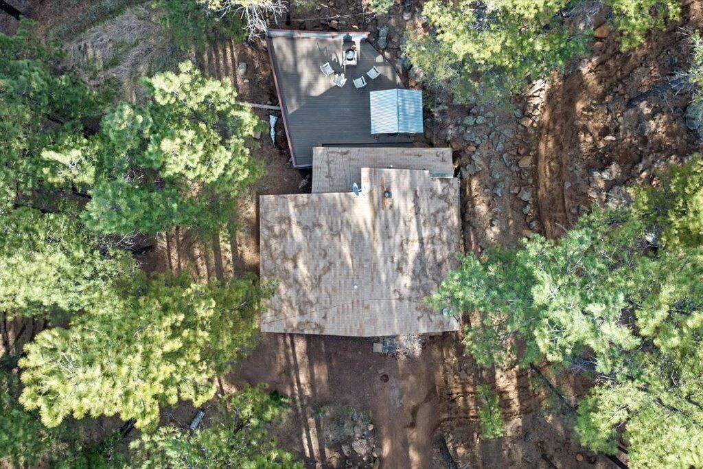 An aerial view of a cabin with a deck, surrounded by dense forest.