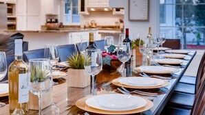 Un tavolo da pranzo apparecchiato con bicchieri da vino, piatti e una bottiglia di vino in una cucina moderna con pensili bianchi e vista sull'esterno.