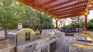 Una cucina esterna con rivestimento in pietra, una griglia integrata e un pergolato.