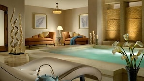 A spa area with a pool, a lounge chair, a sofa, and decorative elements like candles and flowers.