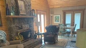 Una sala de estar acogedora con chimenea de piedra, sofá de cuero y comedor con mobiliario de madera.