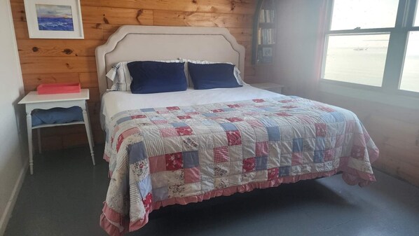 A bedroom with a bed, a nightstand, a window, and a wooden wall.