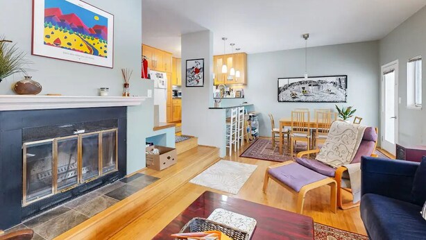 A modern living room with a fireplace, a dining area with a table and chairs, and a kitchen in the background.