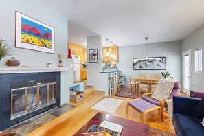 A modern living room with a fireplace, a dining area with a table and chairs, and a kitchen in the background.