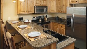 A kitchen with wooden cabinets, a granite countertop, a stainless steel refrigerator, and a built-in oven. - Equipped Suite | Sauna + Spa Access (Park City)