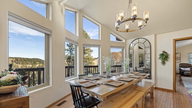 A dining area with a large wooden table set for six, surrounded by black chairs, large windows offering a view of a mountainous landscape, and a chandelier above. - Adventures-Historic Deadwood- Trails- ATV- Skiing-Trolly-Private Acreage (Deadwood)