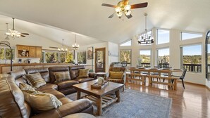 A spacious living area with a large leather sectional sofa, a wooden coffee table, and a dining table with benches. There are ceiling fans, pendant lights, and large windows offering a view of the outdoors. - Adventures-Historic Deadwood- Trails- ATV- Skiing-Trolly-Private Acreage (Deadwood)