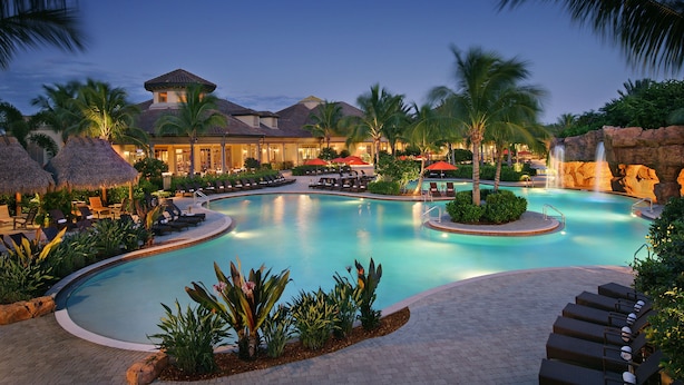 Ein Poolbereich eines Resorts mit Liegestühlen, Palmen und einem Gebäude mit einem Ziegeldach.