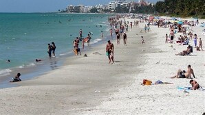 Ein voller Strand mit Menschen, die sich sonnen und schwimmen.