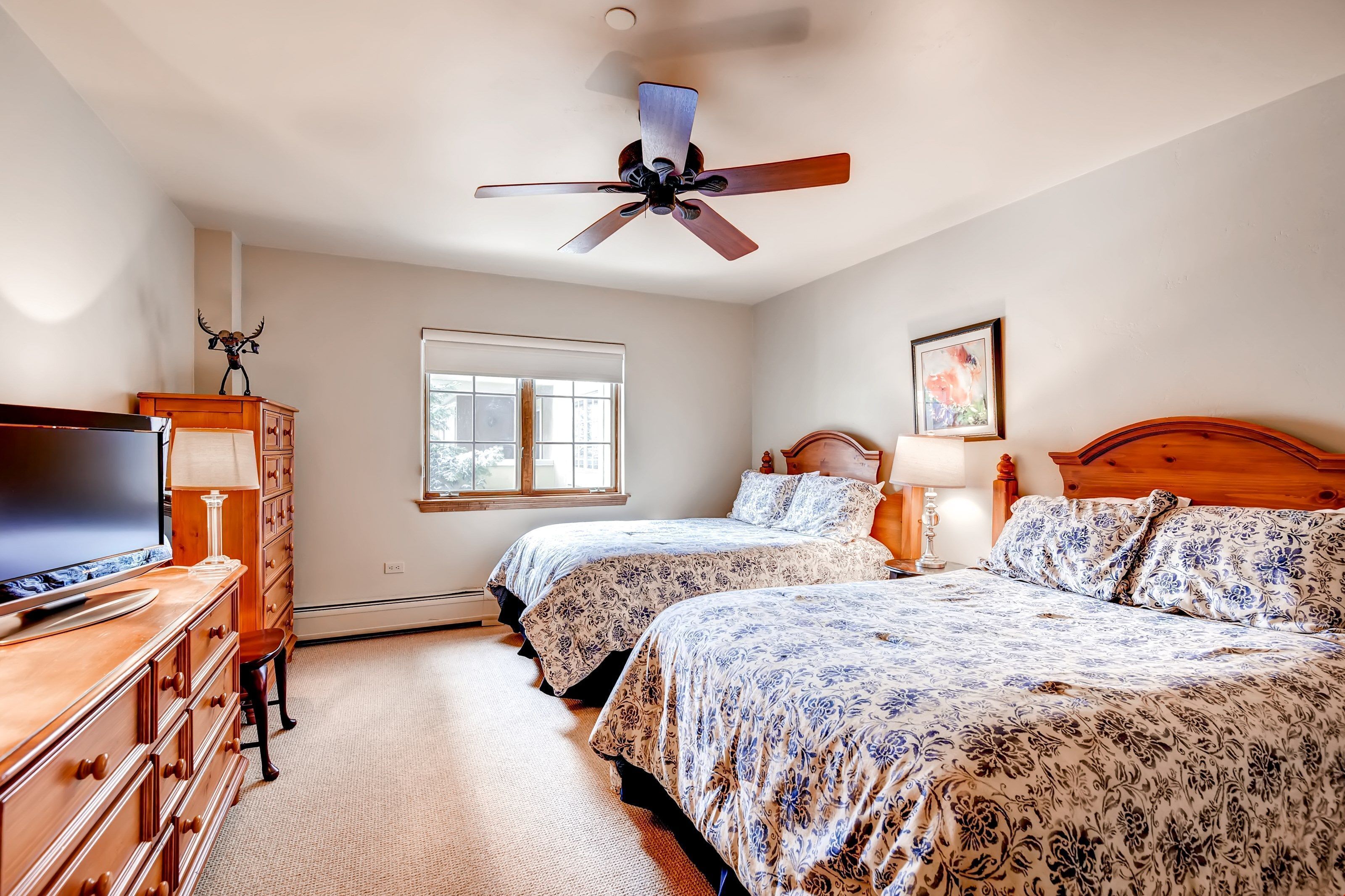 A bedroom with two beds, a TV, a dresser, a ceiling fan, and a window.