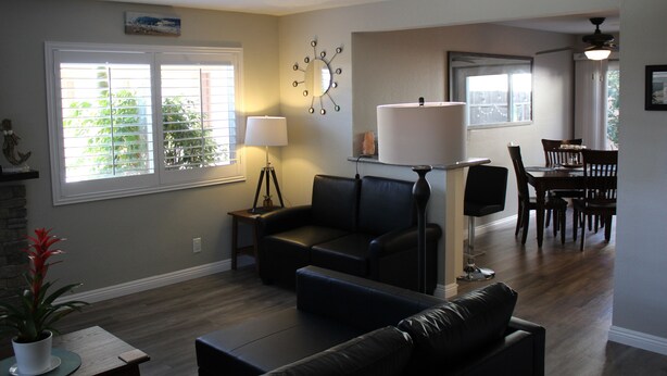 A living room with a sofa, a coffee table, a lamp, and a dining area with a table and chairs. - Huntington Beach Townhome style apartment, close to pier, beach and Pacific City (Huntington Beach)