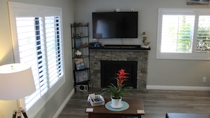 A living room with a fireplace, a television mounted above it, and a bookshelf. - Huntington Beach Townhome style apartment, close to pier, beach and Pacific City (Huntington Beach)