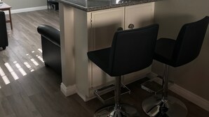 A modern kitchen with a granite countertop, two bar stools, a built-in island, and a stone fireplace. - Huntington Beach Townhome style apartment, close to pier, beach and Pacific City (Huntington Beach)
