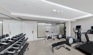 A modern gym with various exercise equipment including dumbbells, a stationary bike, a treadmill, and a bench. - Tulsa Club Hotel, Curio Collection by Hilton (Tulsa)
