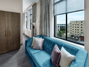 A modern living room with a blue sofa, a wooden wardrobe, and a large window offering a city view. - Tulsa Club Hotel, Curio Collection by Hilton (Tulsa)