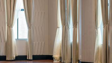 Una habitación con ventanas amplias, cortinas color beige y suelo de madera.