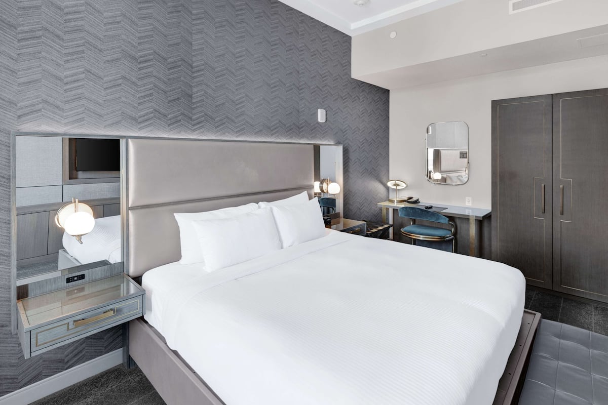 A modern hotel room with a large bed, bedside tables, a desk, and a wardrobe.