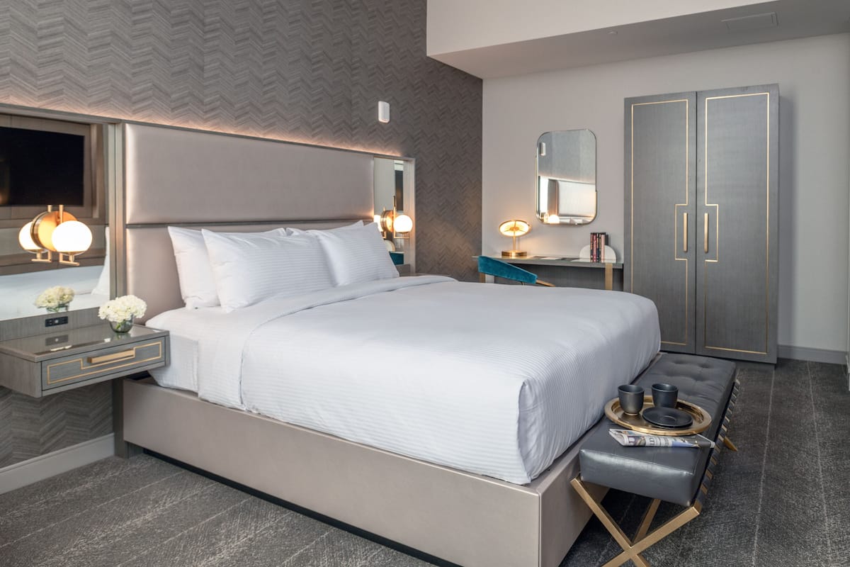 A modern hotel room with a large bed, bedside tables, a vanity with a mirror, and a wardrobe.