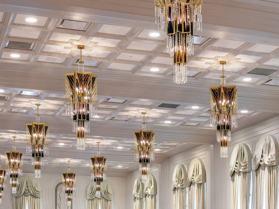 Habitació luxosa amb ostentosos candelabres, un sostre alt amb il·luminació empotrada i cortines elegants penjades.