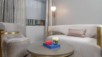 A modern hotel room with a grey sofa, a round coffee table with a vase of white flowers, and a red and blue book.