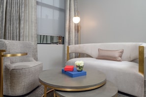 A modern hotel room with a grey sofa, a round coffee table with a vase of white flowers, and a red and blue book. - Tulsa Club Hotel, Curio Collection by Hilton (Tulsa)