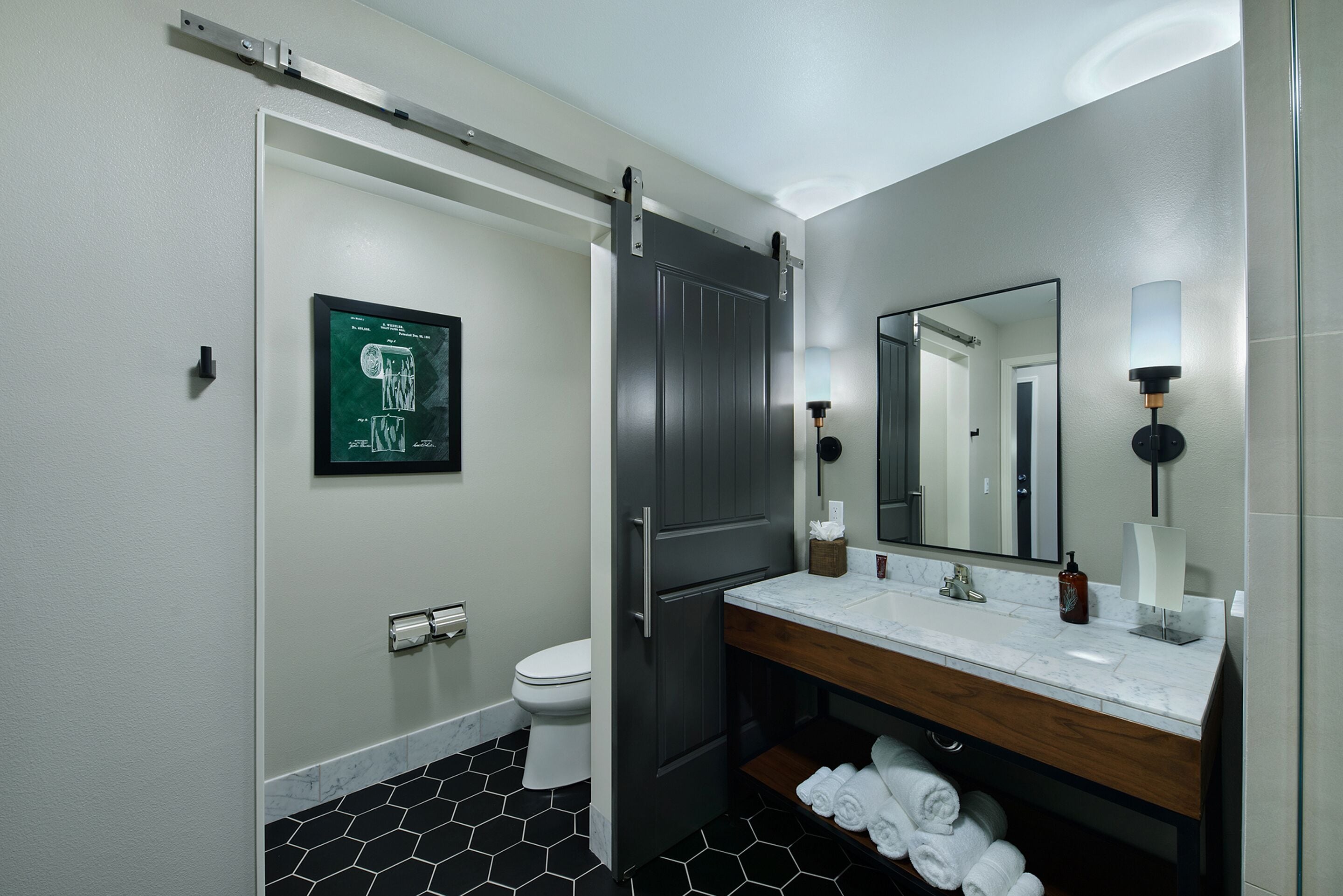Un bagno moderno con porta scorrevole, un WC, un lavabo con piano in marmo, uno specchio e un portasciugamani.