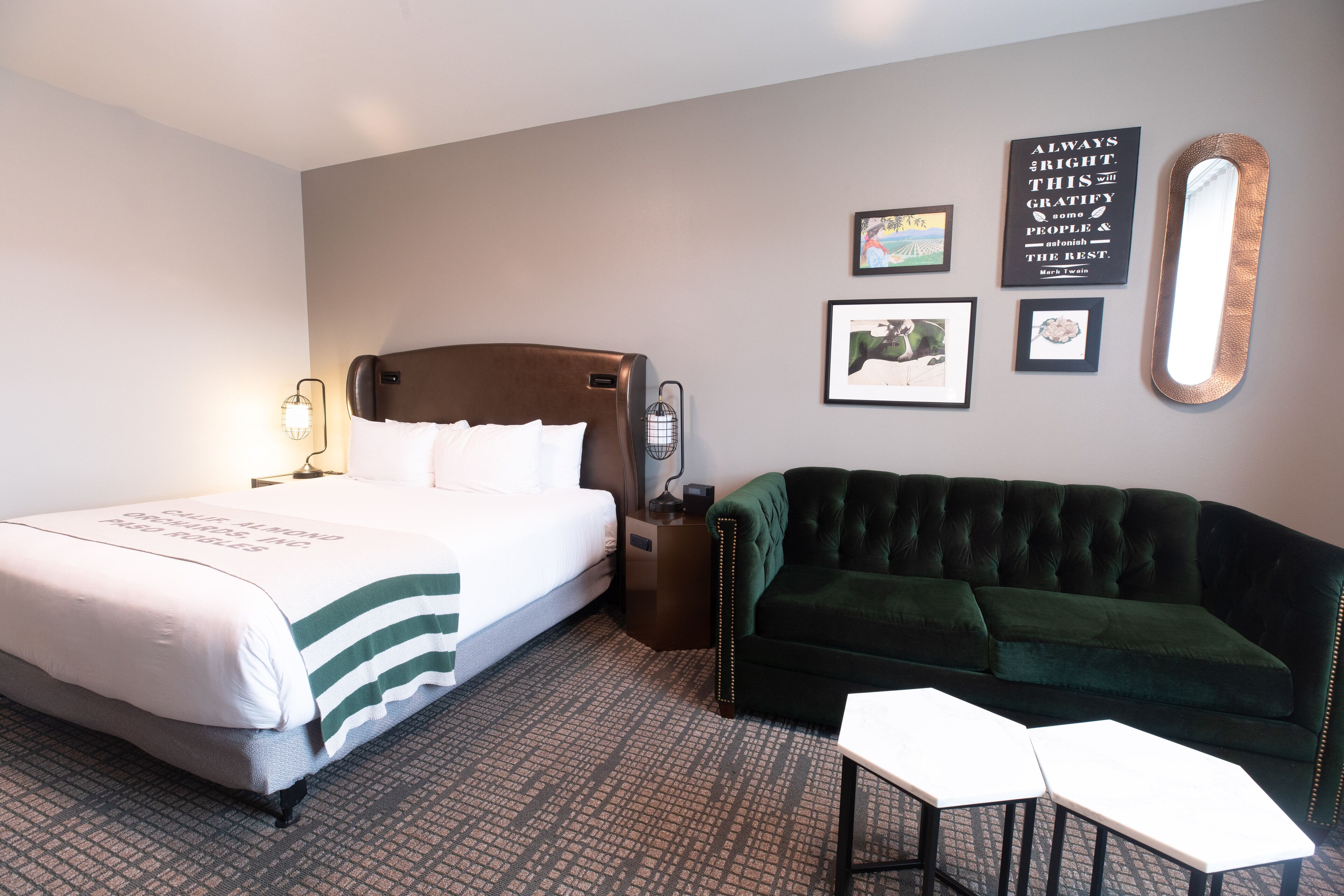 A hotel room with a bed, a green sofa, two white tables, and framed pictures on the wall.