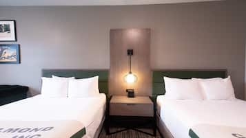 A hotel room with two beds, a nightstand with a lamp, and a wall-mounted light fixture.