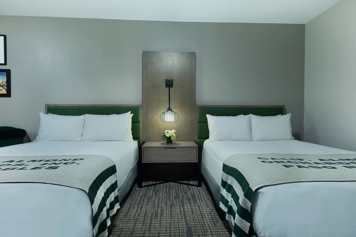 A hotel room with two beds, a nightstand with a lamp, and a green and white striped bedspread.