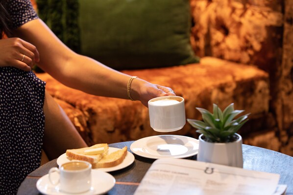 A person holding a cup of coffee, with a plate of toast and a small plant on a table. - Oxford Suites Paso Robles (Paso Robles)