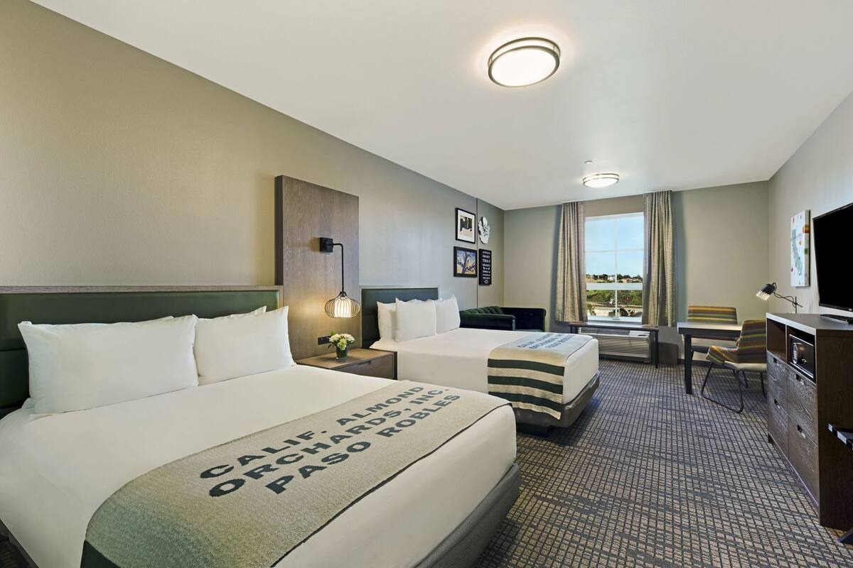 A hotel room with two beds, a desk, a chair, a television, and a window with a view.