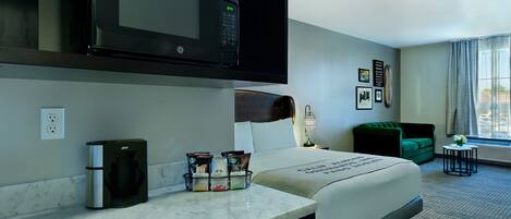 A hotel room with a bed, a microwave, a coffee maker, and a small table with a flower vase.