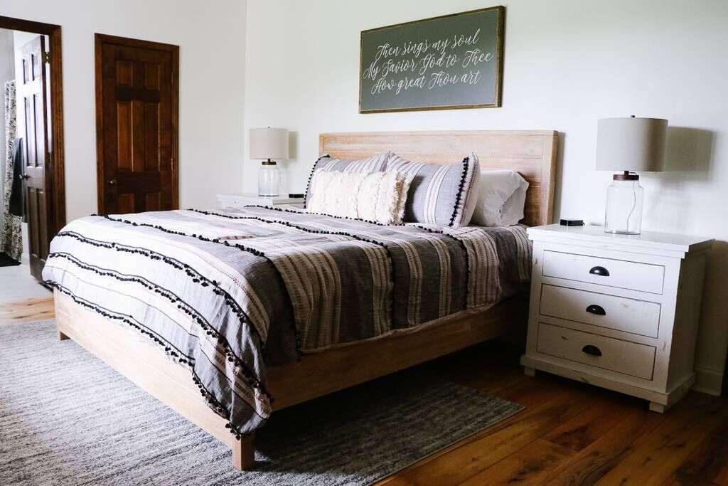 A neatly arranged bedroom with a wooden bed, two bedside tables, a nightstand, a wall-mounted lamp, and a motivational quote on the wall.