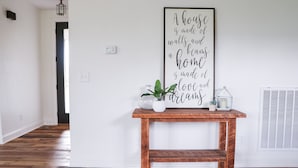 Een hal met een houten vloer, een houten bankje, een muur met een inspirerende quote en een raam met jaloezieën.