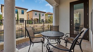A balcony with a round table and four chairs, a glass door, and a view of neighboring houses.