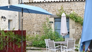 A stone building with a rustic charm, featuring a table and chairs under a blue umbrella, and a red fence in the foreground. - Domaine Les Granges (Ternant)