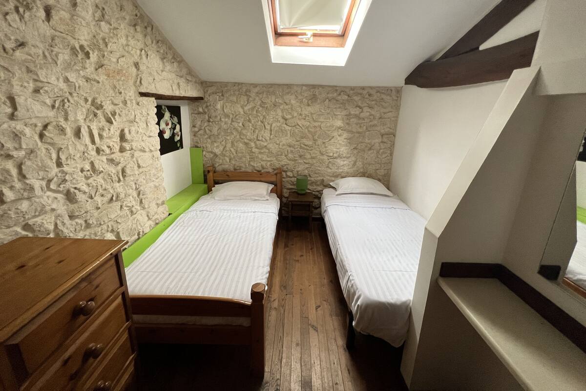 A small, rustic room with two wooden beds, a wooden dresser, and a stone wall.