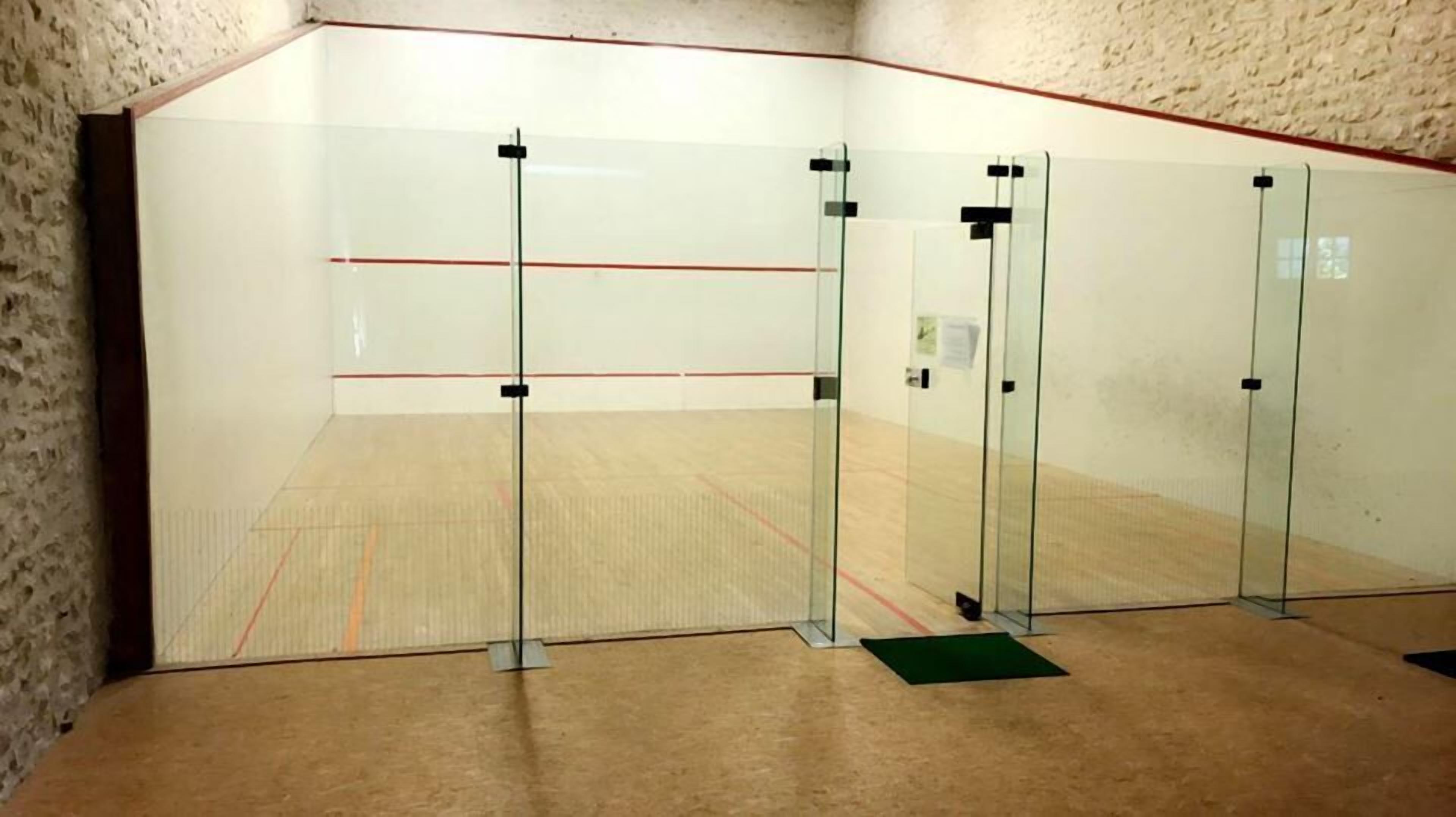 Un court de squash avec des murs en verre, un plancher en bois et une ligne rouge délimitant la zone de jeu.