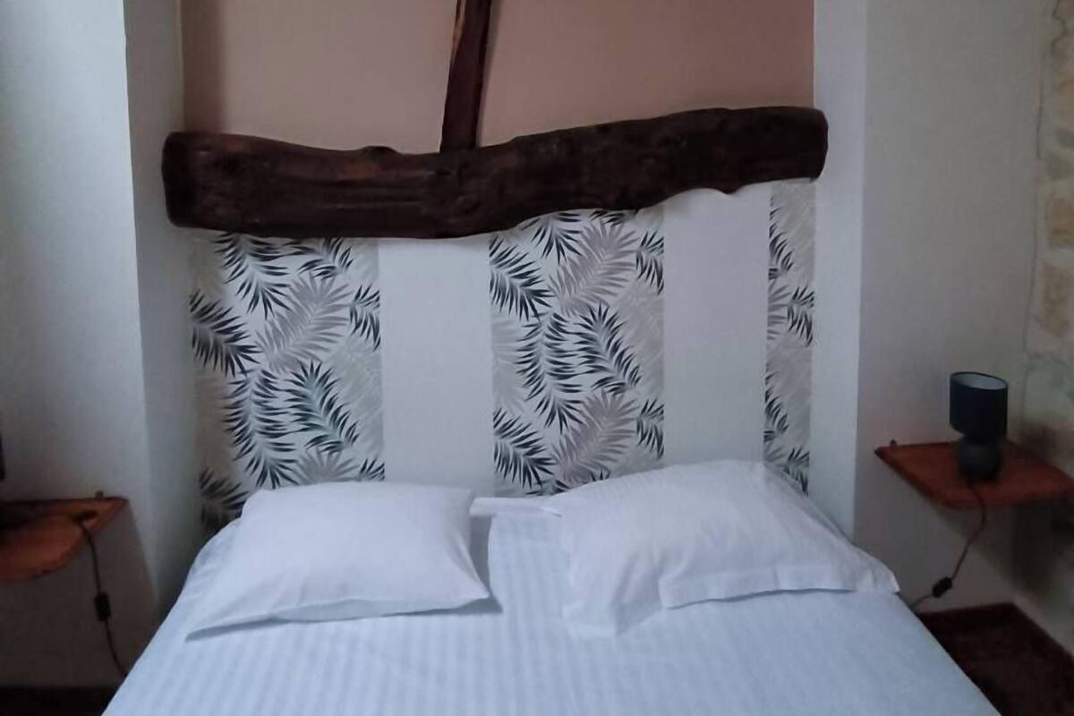 A bed with a headboard featuring a leaf pattern, a wooden beam above the bed, and a nightstand with a lamp.